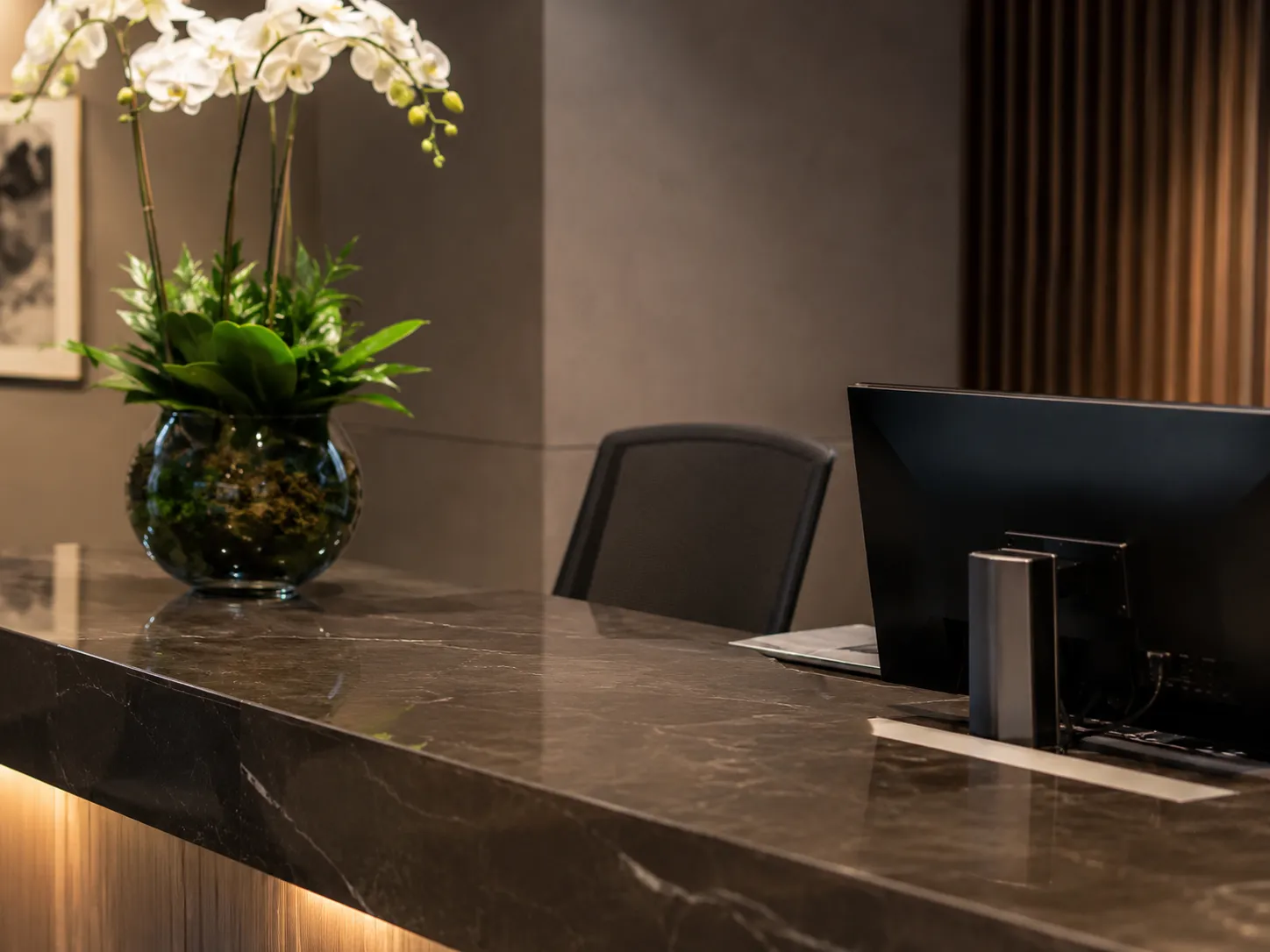 Polished marble reception desk with orchids and a monitor in a contemporary office foyer